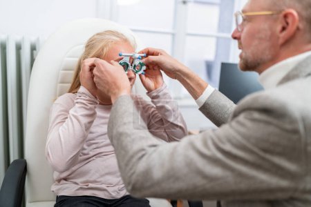 Optometrist fitting Optical measuring glasses on a young blonde girl during an eye exam at the ophthalmology clinic.