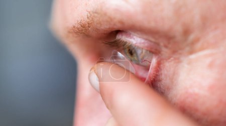 man putting contact lens in his right eye, close up