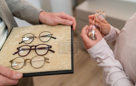 Close-up of hands presenting various eyeglasses on a tray in a optician store.