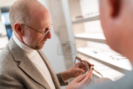 Foto de Óptico mostrando anteojos a cliente mayor en tienda óptica - Imagen libre de derechos