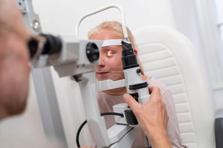 Eye examination with young patient looking into an optometry machine or tonometer at eye clinic