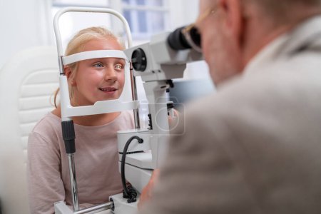 Examen des yeux avec une jeune fille regardant dans une machine d'optométrie à la clinique oculaire