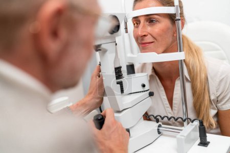 Foto de Optometrista sometida a un paciente a un examen ocular con un enfoque en su ojo iluminado utilizando una lámpara de hendidura en la clínica. Fotografía de cerca. Concepto de salud y medicina - Imagen libre de derechos