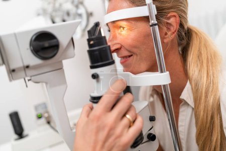 Foto de Paciente femenina sometida a un examen ocular con foco en su ojo iluminado utilizando una lámpara de hendidura en la clínica. Fotografía de cerca. Concepto de salud y medicina - Imagen libre de derechos