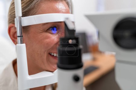 Photo for Smiling woman during eye exam with retinal reflection visible using a slit lamp at the clinic. Close-up photo. Healthcare and medicine concept - Royalty Free Image