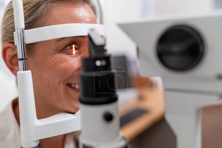 Photo for Smiling woman during eye exam with slit-lamp retinal reflection visible at the ophthalmology clinic. Close-up photo. Healthcare and medicine concept - Royalty Free Image