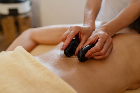 Nahaufnahme einer Hot-Stone-Massage auf nacktem Rücken mit den Händen des Therapeuten im Schönheitssalon oder Hotel