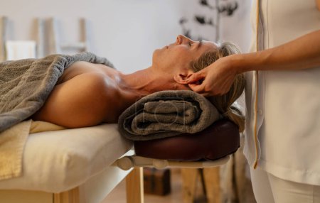 Seitenansicht einer Massagetherapeutin bei einer Ohrenmassage für eine entspannte Kundin