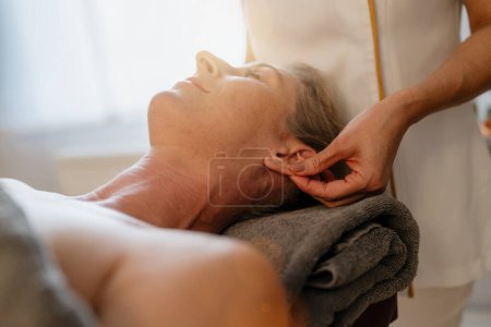 Seitenansicht einer Massagetherapeutin bei einer Ohrenmassage für eine entspannte Kundin in einem Schönheitssalon
