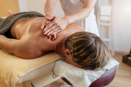 Therapeutin gibt einem männlichen Klienten in einem Wellness-Resort oder Schönheitssalon eine tiefe Geweberückenmassage