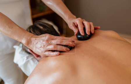 Massagetherapeutin verwendet heiße Steine auf dem Rücken des Klienten während einer Wellness-Behandlung
