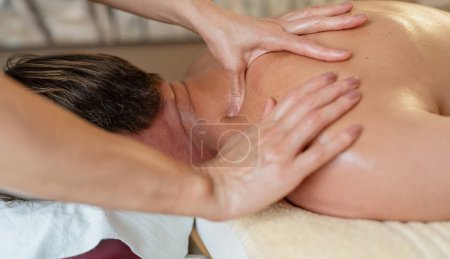 Close-up of hands massaging a man's shoulder blades and back in a spa setting