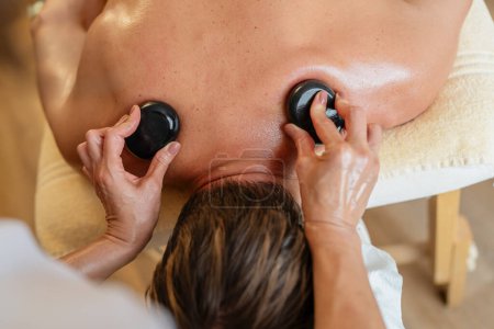 Hände, die einem Kunden während einer Massage in einem Wellness-Hotel heiße Steine auf den Rücken legen