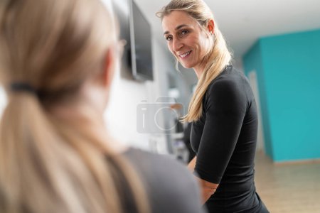 Customer in a gym has a conversation with a trainer during a check-up, she is smiling and cheerful.