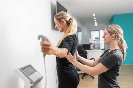 Trainer, der einen Klienten auf einer medizinischen Skala der Körperzusammensetzung bei einem Inbody-Test in einem Fitnessstudio unterstützt, beide lächelnd.