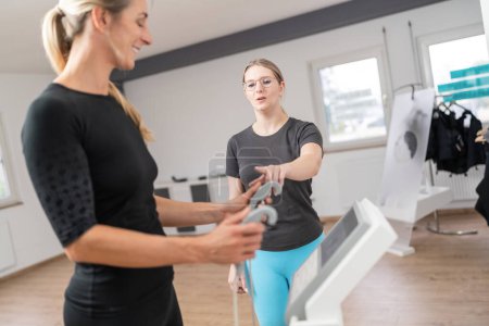 Trainer explaining body composition scale for Inbody analysis test  client holding handles in a fitness studio, both looking engaged.