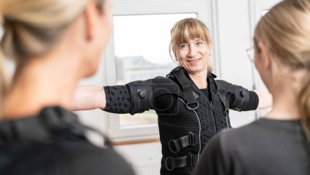 mujer está siendo asistida con el montaje de un traje de entrenamiento EMS por un entrenador en un moderno EMS-Studio