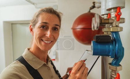 Lächelnde Heizungsingenieurin in einem Gas-Heizungsraum mit Checkliste auf einem Klemmbrett. Konzept zum Austausch von Gasheizungen