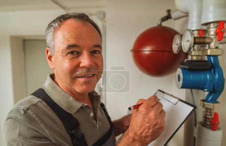 Foto de Ingeniero que controla las tuberías de calefacción en la sala de calderas de gas con lista de verificación en un portapapeles. Imagen del concepto de obligación de sustitución del calentador de gas - Imagen libre de derechos