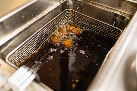 fried potato balls deep frying in deep frying fat at a commercial kitchen of a restaurant. Luxury hotel cooking concept image.