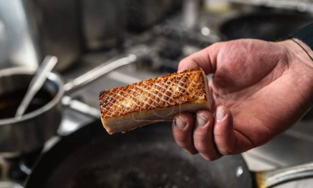 Hand holding a Crispy pork belly which was roasted in a hot pan in a professional kitchen at a restaurant. Luxury hotel cooking concept image.