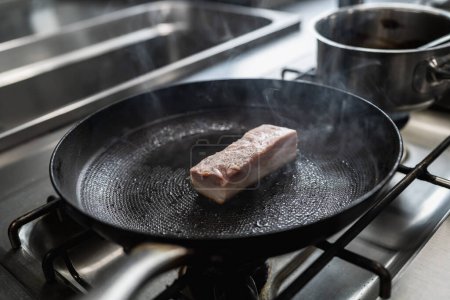 Foto de Cerdo crudo Asado en sartén caliente con aceite en una estufa de gas en una cocina profesional en un restaurante. Imagen concepto de cocina de hotel de lujo. - Imagen libre de derechos