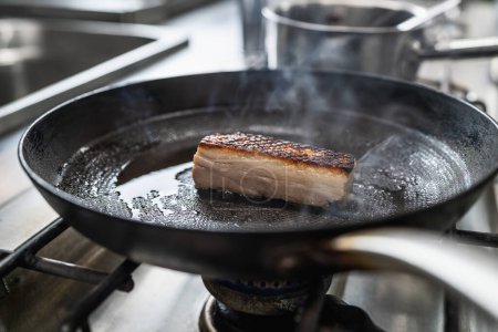 Knuspriger Schweinebauch Braten in heißer Pfanne mit Öl am Gasherd in der professionellen Küche eines Restaurants. Image des Luxushotels.