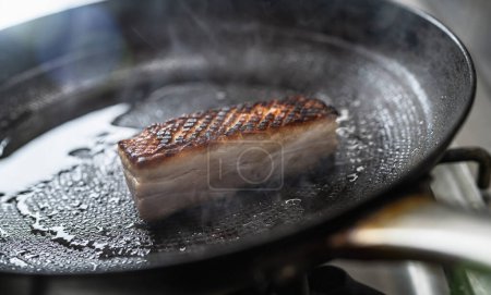 Knuspriger Schweinebraten in heißer Pfanne mit Öl am Gasherd in der professionellen Küche eines Restaurants. Image des Luxushotels.