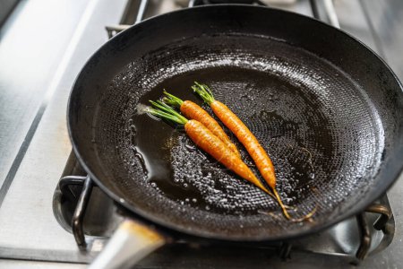 Carrots frying in oiled pan at a gas stove in a professional kitchen at a restaurant. Luxury hotel cooking concept image.