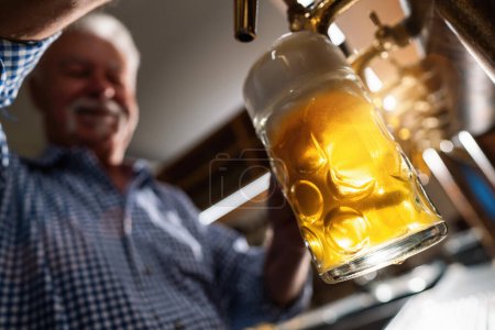 happy bartender in tracht pouring draft beer at german Oktoberfest or Biergarten