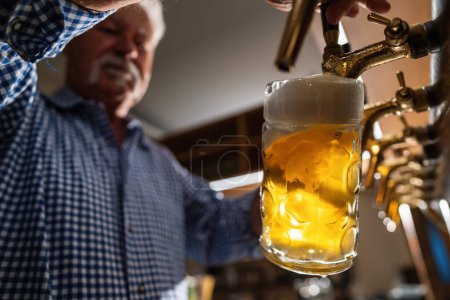traditional bartender in tracht pouring draft beer at german Oktoberfest or Biergarden
