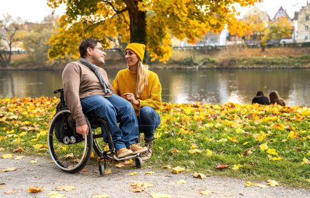 Mujer del servicio social y su amiga en silla de ruedas conversando a través del Riverside en Park en otoño. Imagen de concepto de Momentos de Apoyo