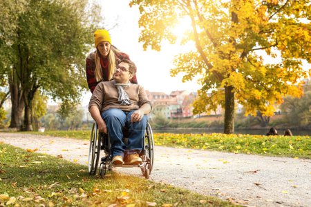 Frau und ihr Freund im Rollstuhl spazieren im Herbst durch den Park am Fluss