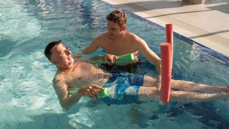 Terapeuta y paciente usando fideos de piscina para ejercicios de rehabilitación en una piscina