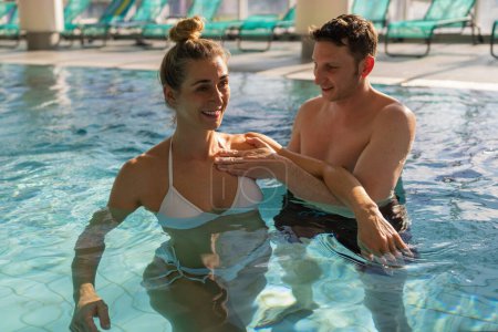 Entrenador masculino asistiendo a una mujer con ejercicios de hombro en una piscina para aeróbicos acuáticos en rehabilitación