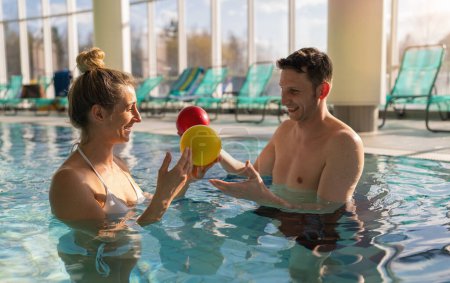 Entraîneur masculin et cliente heureux d'utiliser des boules d'exercice colorées lors d'une séance de thérapie en piscine