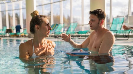 Focused conversation between a male trainer and female client during a pool rehabilitation session