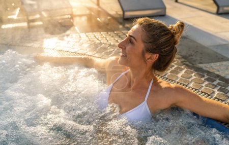 Mujer sonriente relajándose en una bañera de hidromasaje, la luz del sol brillando a través de gotas de agua