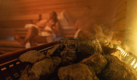 Dampf steigt aus Saunasteinen, im Hintergrund verschwommene Menschen, warmes, glühendes Licht. Entspannung im finnischen Sauna-Wellness-Hotel-Konzept