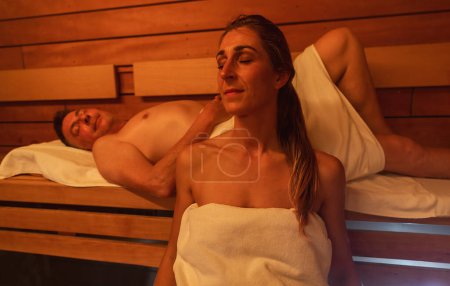woman and a man relaxing in a finnish sauna, man lying down in the background, warm light