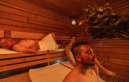 sauna session with a man enjoying a vihta treatment and others relaxing in the wooden room at a finnish sauna. Wellness Spa Hotel Conept image.