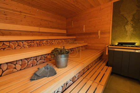 interior de la sauna finlandesa con madera apilada, bancos, un cubo de sauna, vihta (batidores de abedul), y sombreros de fieltro