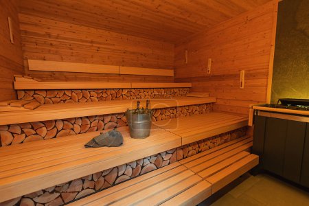 Leerer finnischer Saunaraum mit Holzbänken und -wänden, Saunasteinheizung, Eimer, Schöpfkelle und Filzhüten. Wellness Spa Hotel Konzept.