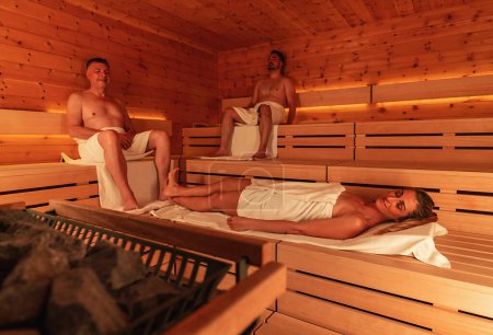 Personas en una sauna finlandesa en un balneario, mujer acostada en primer plano, ambiente cálido de madera
