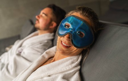 Foto de Mujer con máscara de ojos de gel azul sonriendo, hombre de fondo relajándose en el hotel spa - Imagen libre de derechos