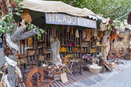 Foto de ALCALA DE HENARES, MADRID, SPAIN - OCTOBER 7, 2016: outdoors shop of wools dyed with natural dyes with several pedal wooden spining wheels and other craft work tools. taken during the celebration of a medieval festival in the streets of the city - Imagen libre de derechos