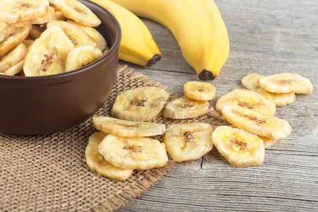 Gesundes Essen - getrocknete Bananenscheiben und frische Bananen auf dem Holztisch. Bananenchips.