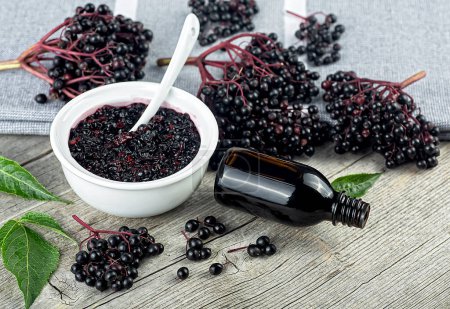 Photo for Delicious homemade black elderberry syrup in glass jar and bunches of black elderberry with green leaves on wooden desk. Sambucus. - Royalty Free Image