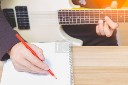 Téléchargez les photos : Auteur-compositeur masculin écrivant une chanson à succès tout en jouant de la guitare électrique blanche. concept d'écriture de chanson - en image libre de droit