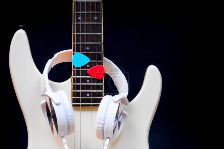 Photo for White headphone on white electric guitar with blue and red picks on black background - Royalty Free Image